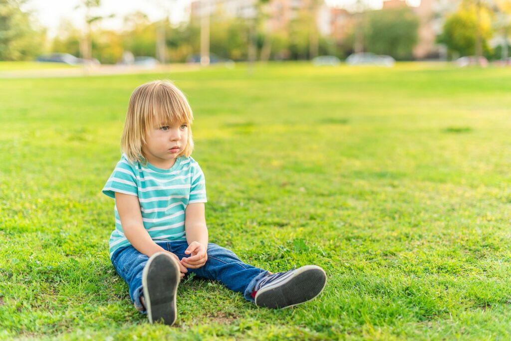 little boy sitting on grass of a park looking away